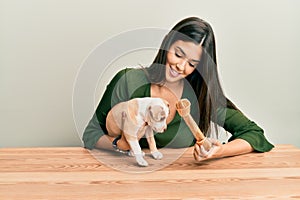 Young hispanic girl smiling happy and playing with dog sitting on the table over isolated white background