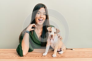 Young hispanic girl smiling happy and playing with dog sitting on the table over isolated white background