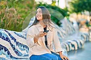 Young hispanic girl smiling happy using smartphone at the park