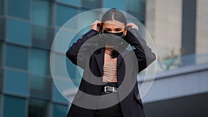 Young hispanic girl standing on city building background looking at camera businesswoman wearing medical protective mask