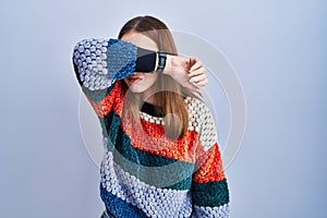 Young hispanic girl standing over blue background covering eyes with arm, looking serious and sad