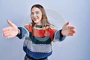 Young hispanic girl standing over blue background looking at the camera smiling with open arms for hug