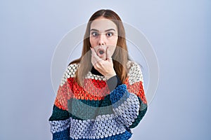 Young hispanic girl standing over blue background looking fascinated with disbelief, surprise and amazed expression with hands on