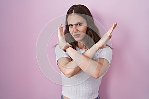 Young hispanic girl standing over pink background rejection expression crossing arms doing negative sign, angry face