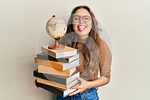 Young hispanic girl studying geography sticking tongue out happy with funny expression