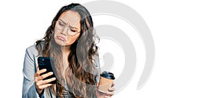 Young hispanic girl using smartphone and drinking a cup of coffee depressed and worry for distress, crying angry and afraid