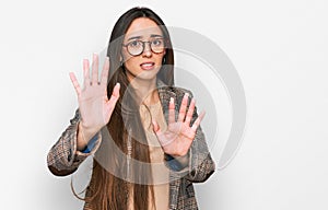 Young hispanic girl wearing business clothes and glasses afraid and terrified with fear expression stop gesture with hands,