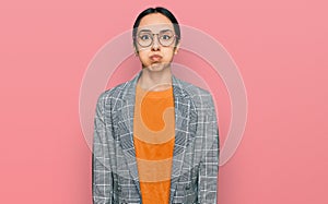 Young hispanic girl wearing business jacket and glasses puffing cheeks with funny face