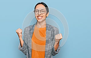 Young hispanic girl wearing business jacket and glasses very happy and excited doing winner gesture with arms raised, smiling and