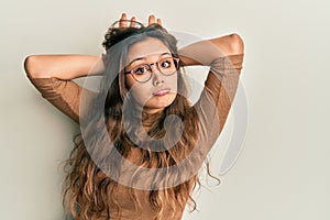 Young hispanic girl wearing casual clothes and glasses doing bunny ears gesture with hands palms looking cynical and skeptical