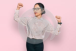 Young hispanic girl wearing casual clothes and glasses showing arms muscles smiling proud