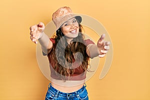 Young hispanic girl wearing casual clothes and hat looking at the camera smiling with open arms for hug