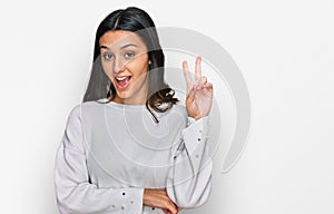 Young hispanic girl wearing casual clothes smiling with happy face winking at the camera doing victory sign