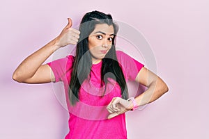 Young hispanic girl wearing casual pink t shirt doing thumbs up and down, disagreement and agreement expression