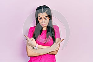 Young hispanic girl wearing casual pink t shirt pointing to both sides with fingers, different direction disagree