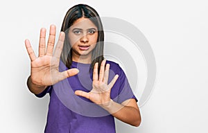 Young hispanic girl wearing casual purple t shirt afraid and terrified with fear expression stop gesture with hands, shouting in