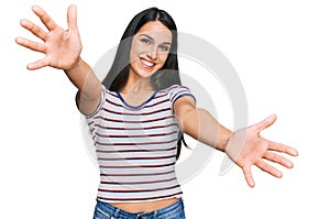 Young hispanic girl wearing casual striped t shirt looking at the camera smiling with open arms for hug