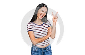 Young hispanic girl wearing casual striped t shirt smiling with happy face winking at the camera doing victory sign