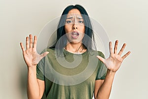 Young hispanic girl wearing casual t shirt afraid and terrified with fear expression stop gesture with hands, shouting in shock