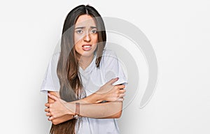 Young hispanic girl wearing casual white t shirt shaking and freezing for winter cold with sad and shock expression on face