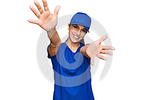 Young hispanic girl wearing delivery courier uniform looking at the camera smiling with open arms for hug