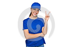 Young hispanic girl wearing delivery courier uniform smiling with happy face winking at the camera doing victory sign