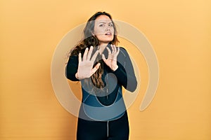 Young hispanic girl wearing diver neoprene uniform afraid and terrified with fear expression stop gesture with hands, shouting in