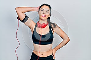 Young hispanic girl wearing gym clothes and using headphones confuse and wonder about question