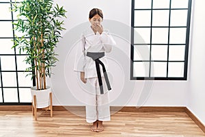 Young hispanic girl wearing karate kimono and black belt bored yawning tired covering mouth with hand