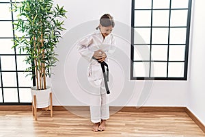 Young hispanic girl wearing karate kimono and black belt with hand on stomach because indigestion, painful illness feeling unwell