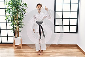 Young hispanic girl wearing karate kimono and black belt pointing finger up with successful idea