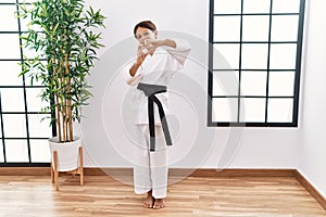 Young hispanic girl wearing karate kimono and black belt smiling in love doing heart symbol shape with hands
