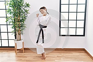 Young hispanic girl wearing karate kimono and black belt very happy and excited doing winner gesture with arms raised, smiling and