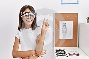 Young hispanic girl wearing optometry glasses smiling with happy face winking at the camera doing victory sign