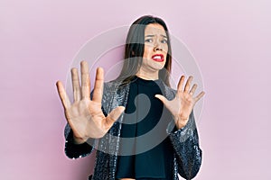 Young hispanic girl wearing party jacket afraid and terrified with fear expression stop gesture with hands, shouting in shock