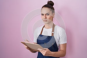 Young hispanic girl wearing professional waitress apron taking order skeptic and nervous, frowning upset because of problem