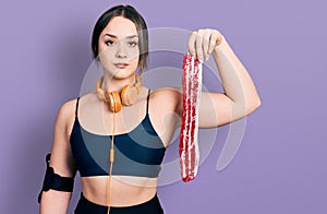 Young hispanic girl wearing sportswear holding meat thinking attitude and sober expression looking self confident