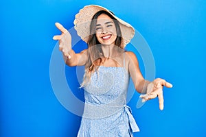 Young hispanic girl wearing summer hat looking at the camera smiling with open arms for hug