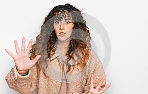 Young hispanic girl wearing winter clothes afraid and terrified with fear expression stop gesture with hands, shouting in shock