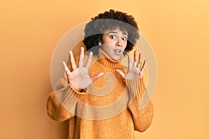 Young hispanic girl wearing wool winter sweater afraid and terrified with fear expression stop gesture with hands, shouting in