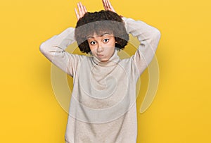 Young hispanic girl wearing wool winter sweater doing bunny ears gesture with hands palms looking cynical and skeptical