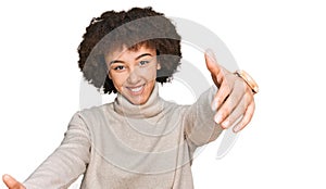 Young hispanic girl wearing wool winter sweater looking at the camera smiling with open arms for hug