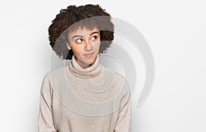 Young hispanic girl wearing wool winter sweater smiling looking to the side and staring away thinking