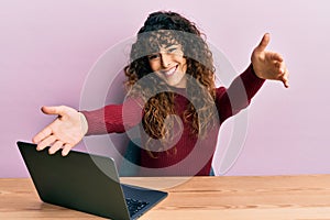 Young hispanic girl working using computer laptop looking at the camera smiling with open arms for hug