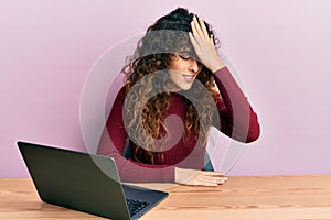 Young hispanic girl working using computer laptop surprised with hand on head for mistake, remember error