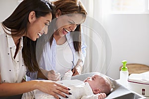 Young Hispanic grandmother and adult daughter playing with her baby son on changing table, close up