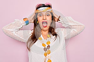 Young hispanic hippie woman wearing fashion boho style and sunglasses over pink background Crazy and scared with hands on head,