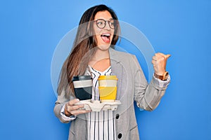 Young hispanic intern business woman holding coffee over blue background pointing and showing with thumb up to the side with happy