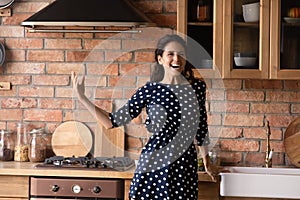 Young hispanic lady singing song aloud by music at kitchen