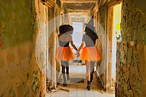 Young Hispanic and Latina women with their backs turned, walking hand in hand down the hallway of a dilapidated building dressed